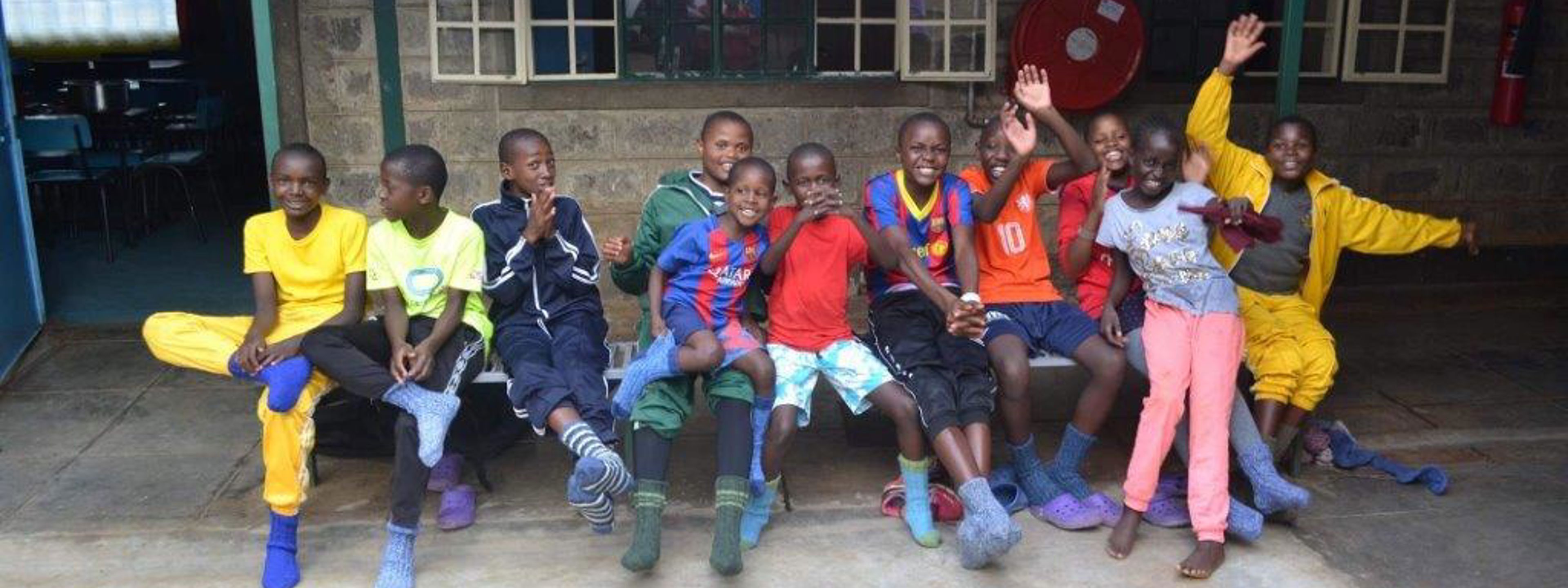 Fleire kenyanske barn sit på ein benk. Barna tuller og ler med kvarandre.