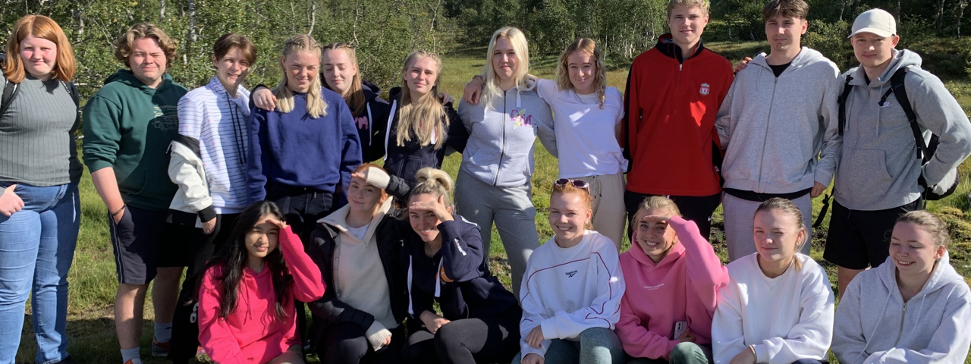 1ST på ekskursjon til Herdla. Elevane sit og står samla, med skog og åsar kring.